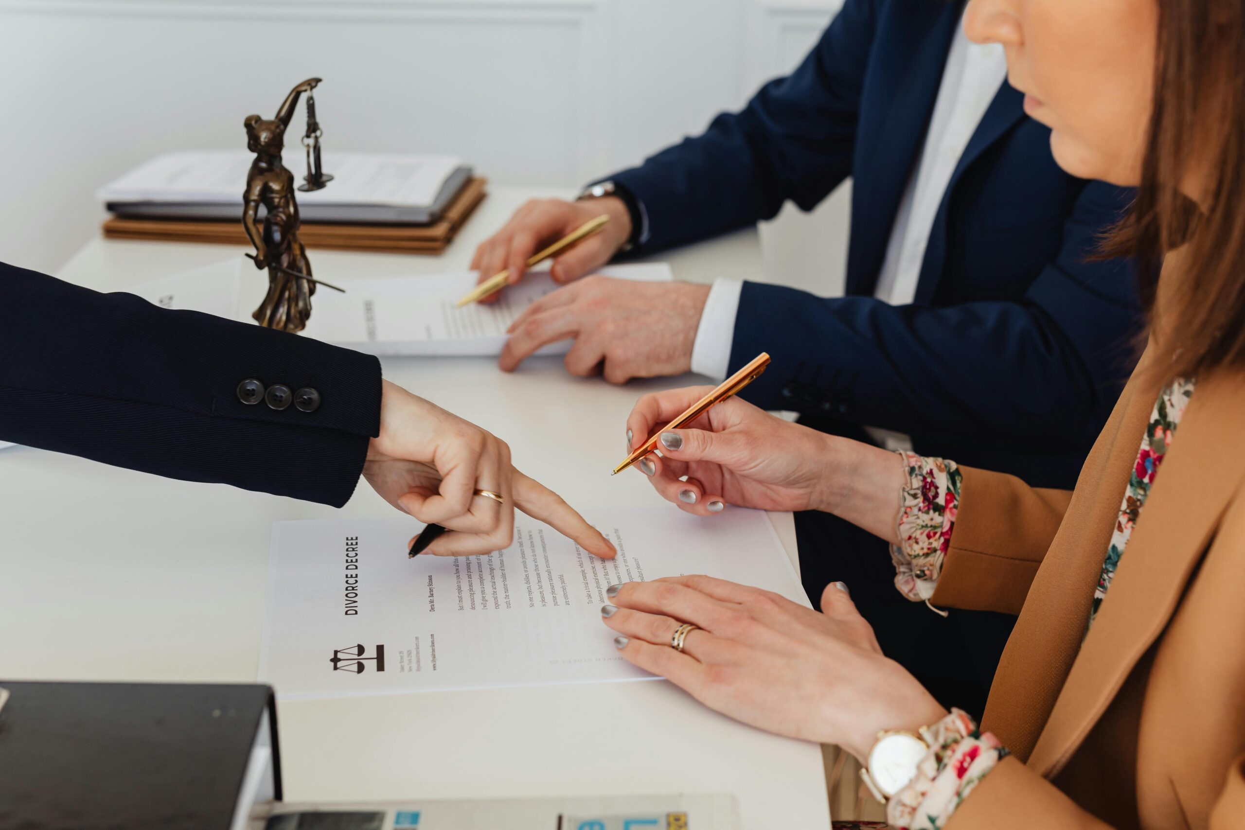 Actualidad Legal Hands signing a divorce decree, with a justice statue nearby, symbolizing legal proceedings.
